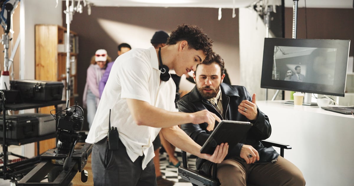 Man, director and producer with tablet for discussion, video edit or retake in production studio. Male people, filmmaker and talking with camera assistant or technology for film making or scene cue