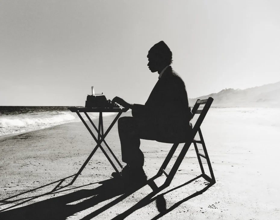 Silhouette of person sitting in chair at beach table with ocean waves in background, black and white photograph